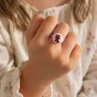 Bague enfant réglable avec motif petit chat rouge sur fond blanc montée sur un anneau argenté.