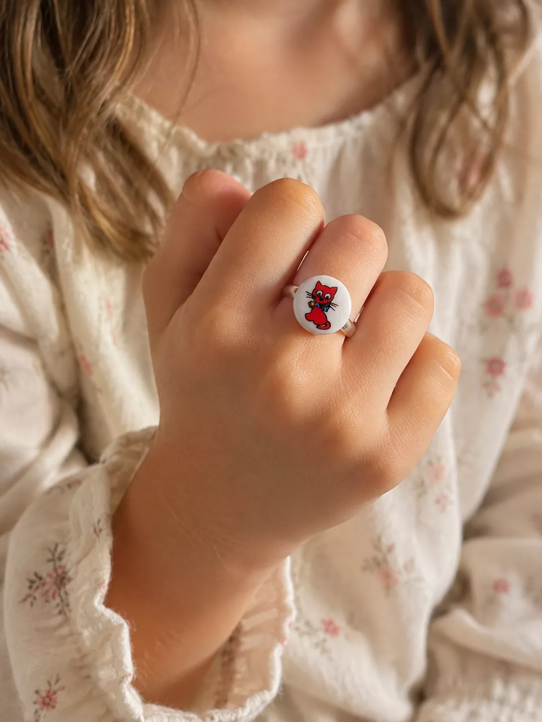 Bague enfant réglable avec motif petit chat rouge sur fond blanc montée sur un anneau argenté.