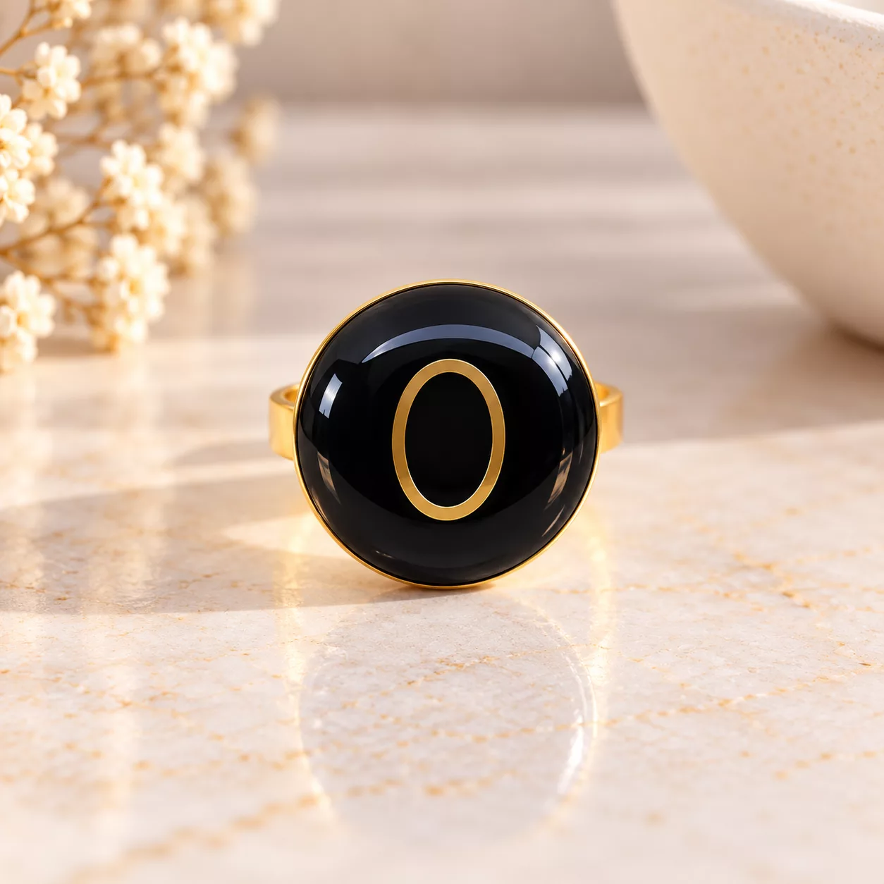 Vue de face de la bague Ô montrant son plateau rond noir brillant et son motif ovale doré