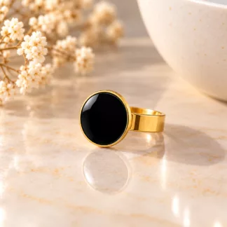 Bague Pastille Noire avec bouton noir brillant et monture dorée sur fond crème