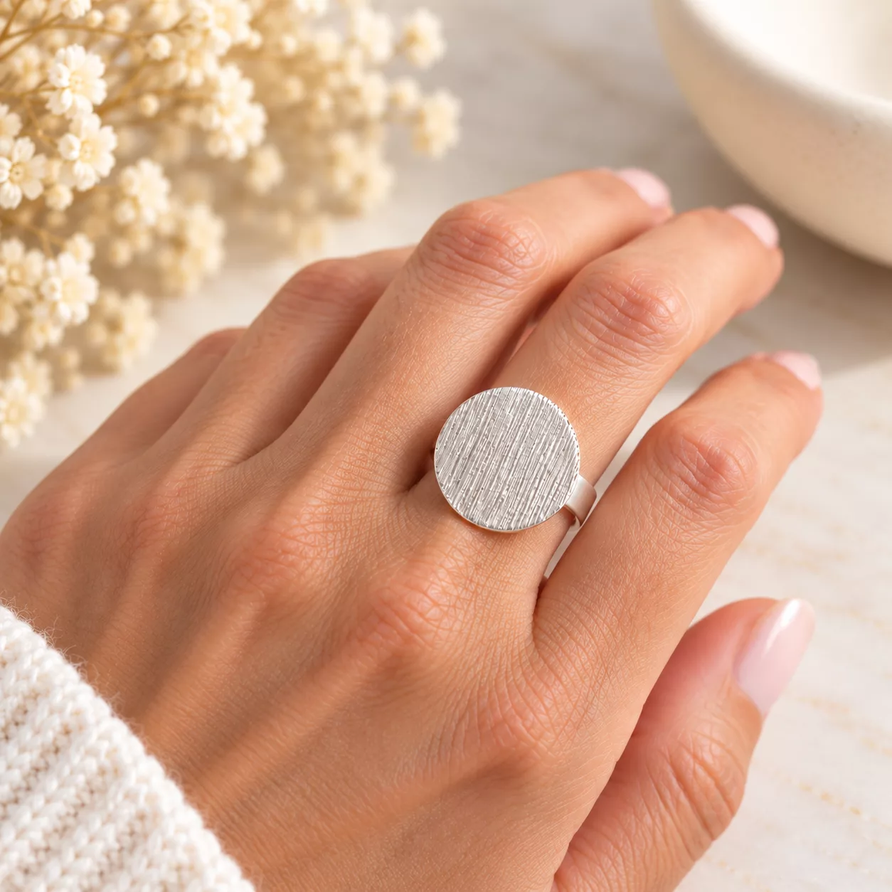Bague argentée minimaliste portée au doigt, avec disque rond à fines stries