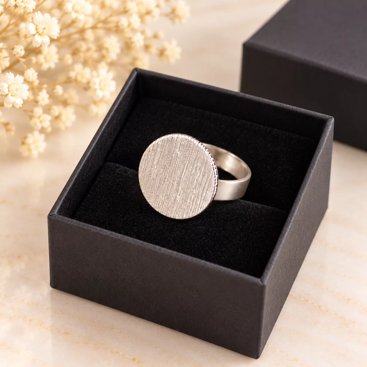 Bague argentée minimaliste au disque texturé présentée dans un écrin cadeau