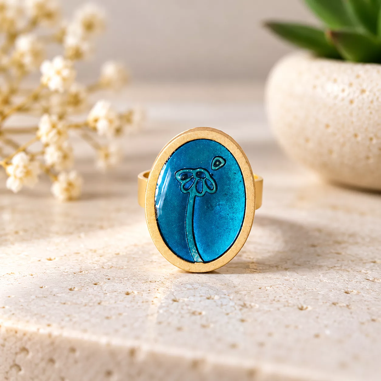 Vue de face du bouton ovale bleu de la bague Beaucoup, à la folie et de son dessin floral