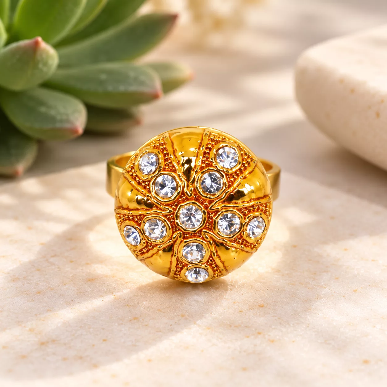 Vue de face du bouton doré de la bague avec strass blancs et motif rayonnant en relief