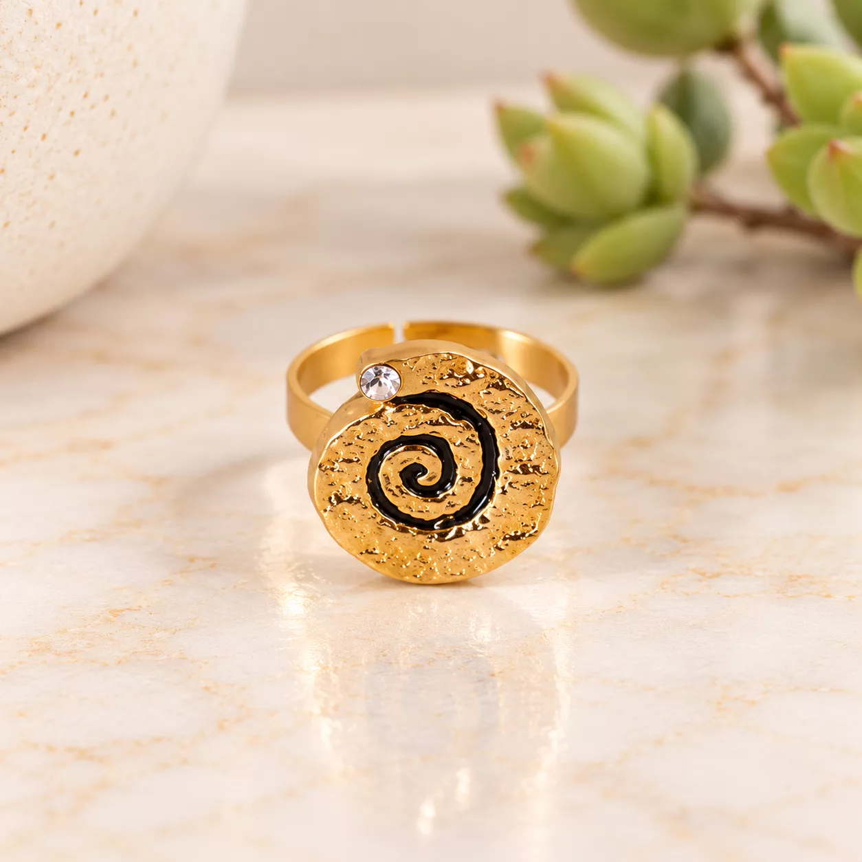 Vue de face de la bague Spirale d’or montrant la spirale noire, le strass et la texture dorée du métal