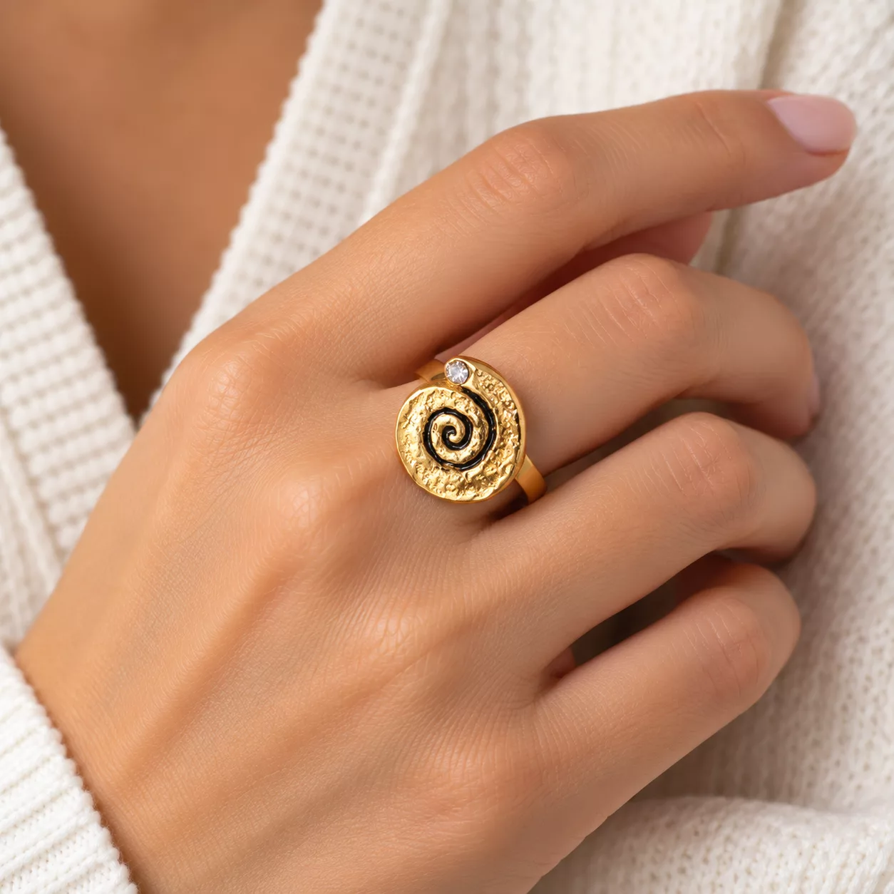 Bague dorée spirale portée à la main, avec motif noir sur métal martelé et petit strass