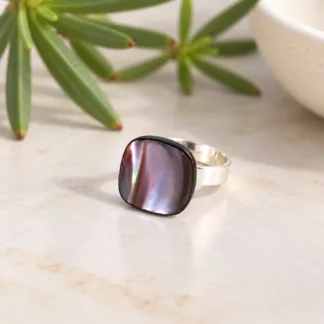 Bague carrée nacrée Mira aux reflets irisés avec anneau argenté sur fond crème