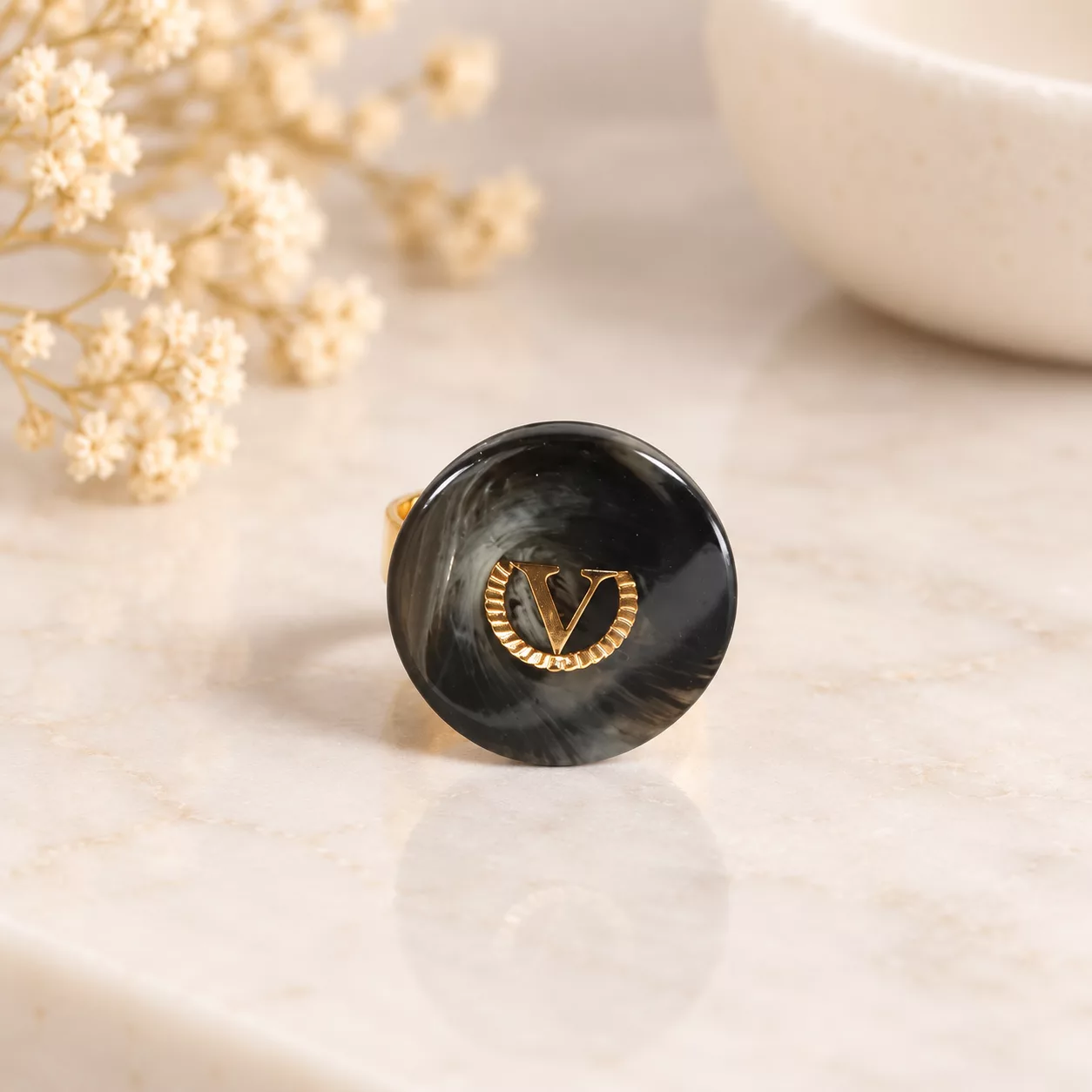 Vue de face de la bague Le V, ancien bouton rond gris anthracite marbré orné d'un V doré