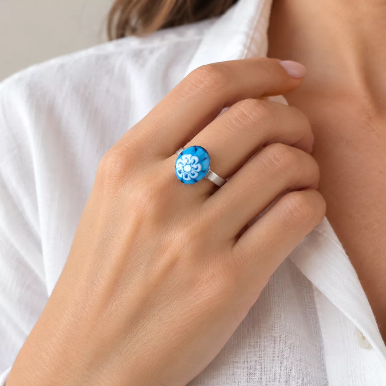 Bague Murano bleue portée au doigt, avec bouton ovale à motif floral blanc