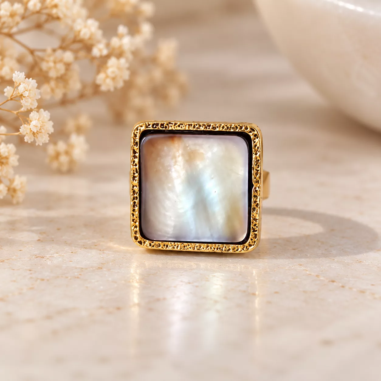 Vue de face de la bague Nacre carrée montrant ses reflets blancs irisés et son contour doré texturé