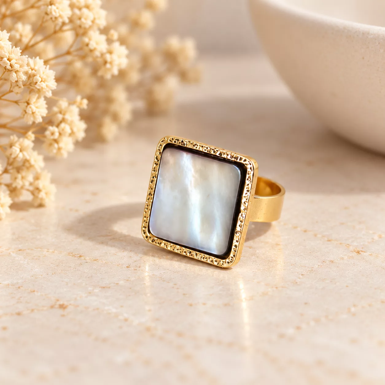 Bague Nacre carrée avec plateau nacré et monture dorée sur fond crème