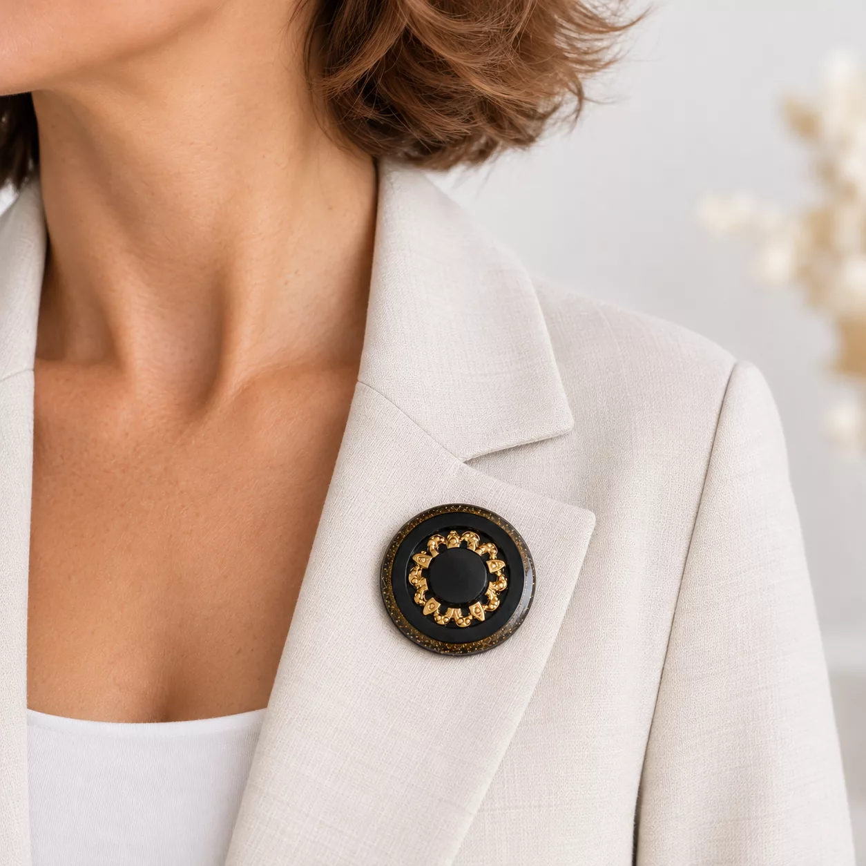 Broche Solstice marron et dorée portée sur le revers d'une veste beige